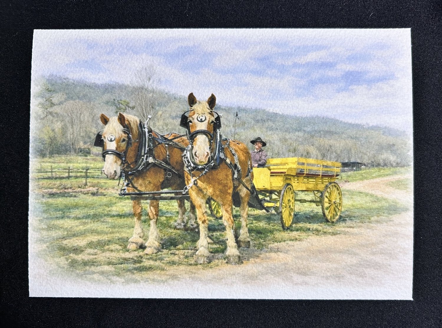 A gicl&eacute;e print of two draft horses in harness pulling a yellow wagon along a dirt road, wooded hills behind, printed on textured 100&percnt; cotton fiber paper.