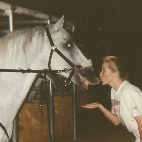 Susannah leaning in to kiss the nose of Precious Pony, a white Lipizzaner, in his stall.