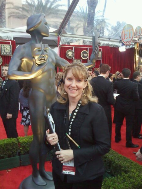 Zuzu smiling on the red carpet at the Screen Actors Guild Awards, beside the giant SAG statue, wearing her production headset and badge.