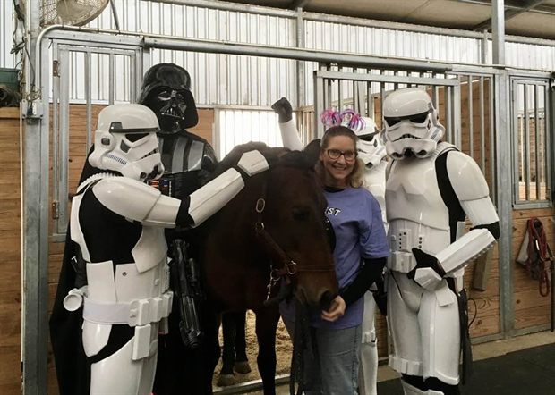 Two stormtroopers and Darth Vader standing with Lovely Rita, a dark horse, in her stable.